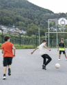 Un groupe de jeunes en train de jourer au foot dehors avec un éducateur